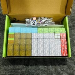 Looking straight down into the open tray: rows of small blocks in brown, blue, white, grey and red, with a sealed bag of parts resting on top.
