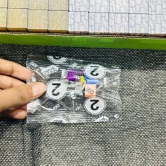 A hand holding up the clear bag of extra parts — round numbered tiles and a few coloured pieces — above the tray of blocks.