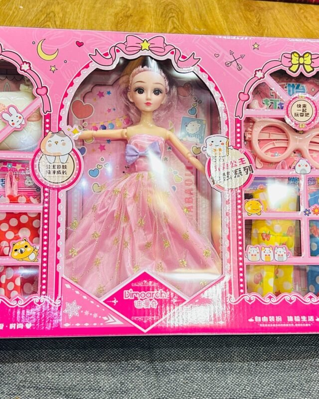 The wide pink box on a grey floor: a doll in a long pink gown stands in the middle window, with trays of hair clips, beads and bows behind the windows either side.