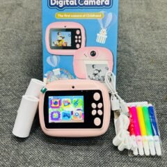 The pink camera standing upright in front of its box, screen lit with the icon menu, a paper roll to one side and the colour pens fanned out to the other.